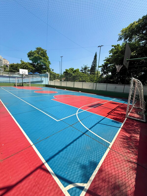 Quadra de basquete ao ar livre com superfície azul e vermelha, um aro e uma rede.