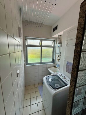 Ein kleines, modernes Badezimmer mit integrierter Waschmaschine und Trockner, einem Fenster mit Blick auf ein grünes Feld und Fliesenwänden.
