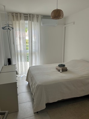 Un dormitorio con cama, mesita de noche, lámpara colgante y ventana con cortinas.