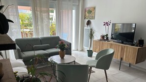 A living room with a sofa, a coffee table, chairs, a TV, and potted plants. - Natura residence near salagou (Clermont-l'Hérault)