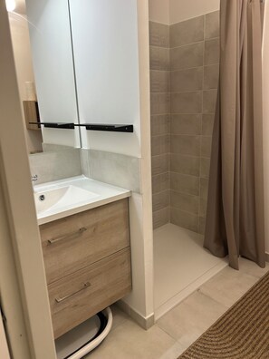 Un baño con lavabo, espejo, tocador de madera y zona de ducha.