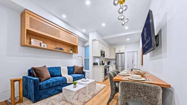 Un salon moderne avec un canapé bleu, une étagère en bois, une table basse en marbre et un coin repas comprenant une table et des chaises.