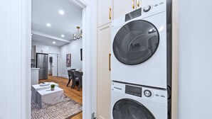 Une buanderie équipée de machines à laver et de sèche-linge superposés, une table basse en marbre et un coin repas avec des chaises et une table.