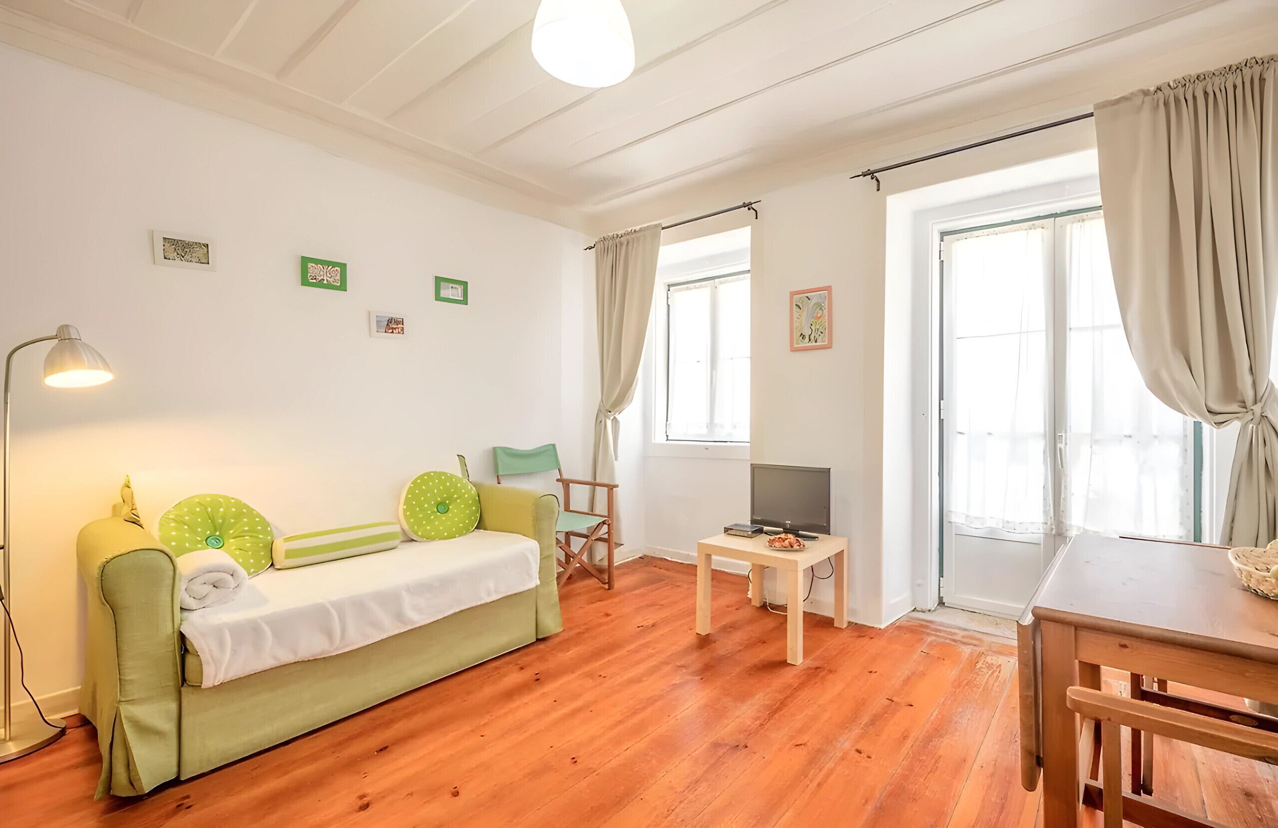 A room with a green sofa, a wooden table, a TV, and a lamp.
