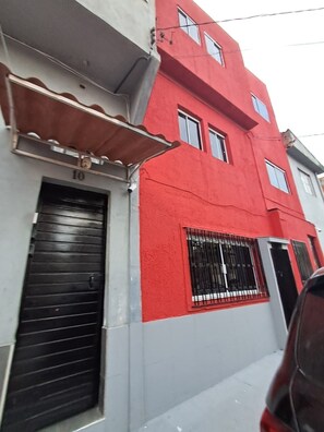 A multi-story building with a red facade, a black garage door, and a metal awning. - Apartamento Confortavel Mobiliado, Zona Norte SP (São Paulo)