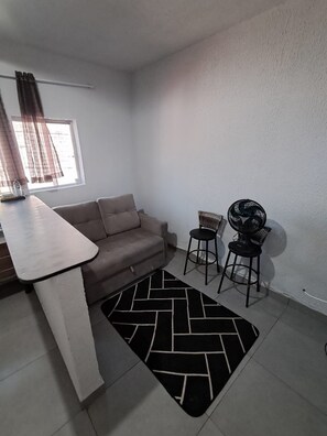 A small, well-lit room with a sofa, a table, two chairs, and a fan. - Apartamento Confortavel Mobiliado, Zona Norte SP (São Paulo)
