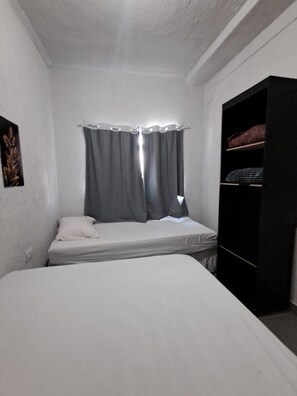 A small, single-bed room with a window covered by curtains, a bedside table, and a wardrobe. - Apartamento Confortavel Mobiliado, Zona Norte SP (São Paulo)