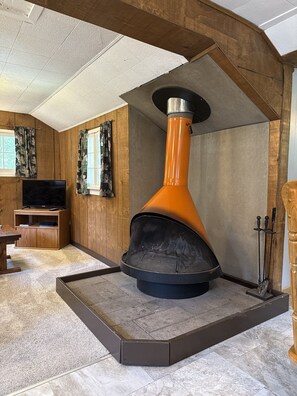 Ein Zimmer mit Kamin, Holzwänden, Fernseher und Esstisch.