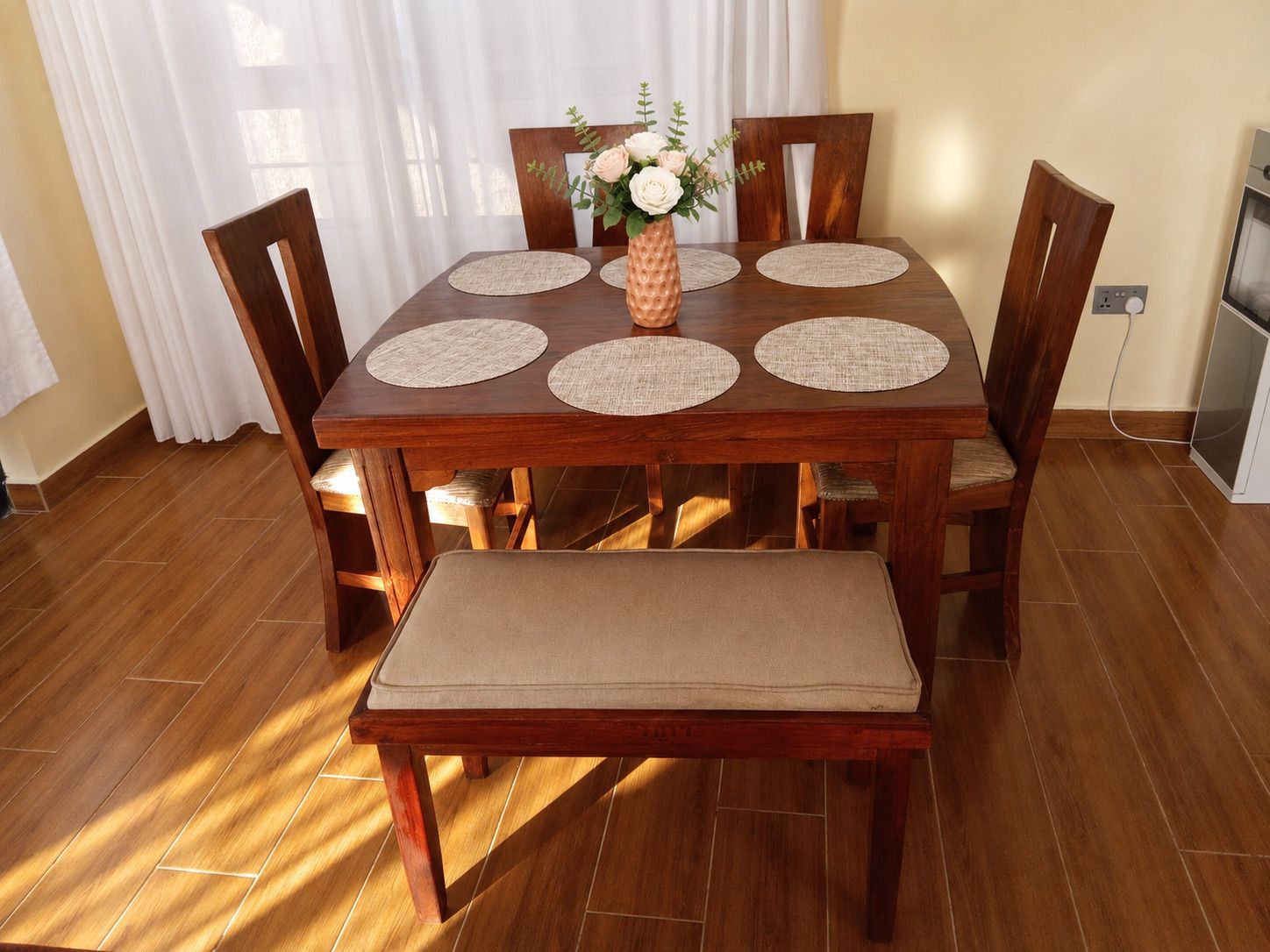 A wooden dining table with four chairs, a bench, and a vase with flowers.