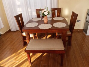A wooden dining table with four chairs, a bench, and a vase with flowers.