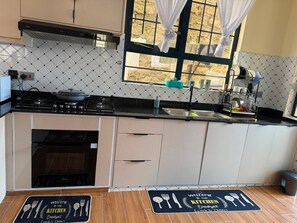 A kitchen with a stove, sink, and cabinets, a window with curtains, and a welcome mat on the floor.