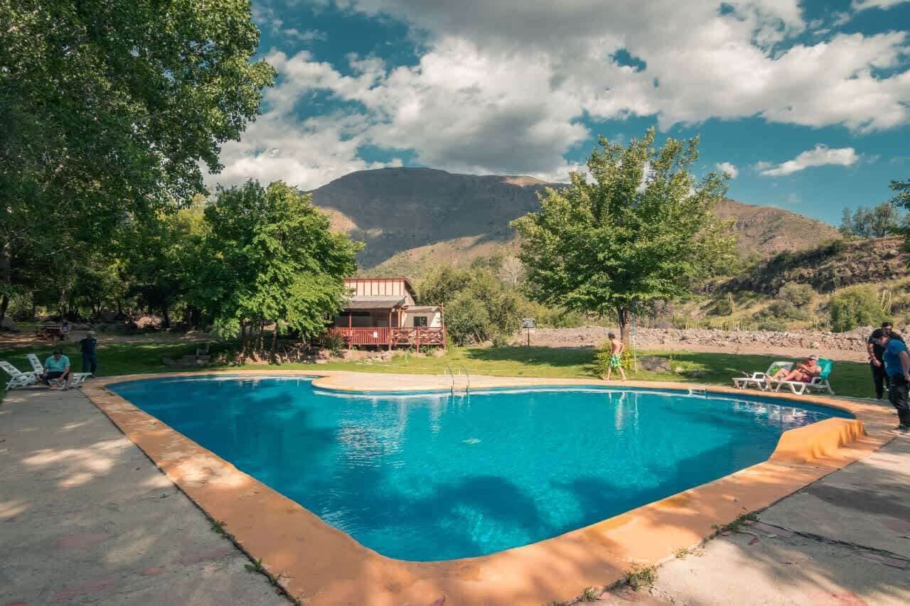 A swimming pool with a wooden deck, surrounded by trees and a mountain backdrop.. Hab compartida 10 personas Wifi Tinajas Cocina