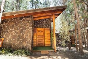 A rustic wooden cabin with a stone exterior, a wooden door, and a green mat at the entrance.