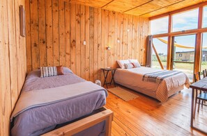 Une cabane en bois avec deux lits, une table Ă manger et de grandes fenĂȘtres.