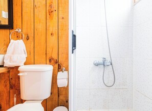 Une salle de bain avec un mur en bois, des toilettes blanches, un porte-serviettes et une douche Ă©quipĂ©e dâun pommeau de douche amovible.