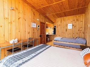 A wooden cabin room with a bed, a desk, and a chair.