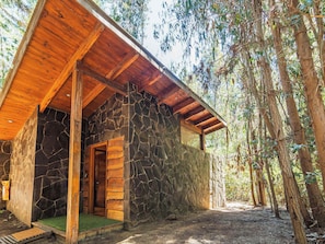 A rustic stone building with a wooden porch and a natural forest backdrop.