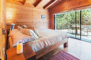 A wooden-paneled bedroom with a bed, pillows, a bedside table, and a lit candle.