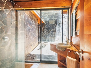 A bathroom with a stone wall, a wooden bench, a sink, and a towel rack.