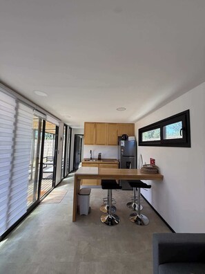 A modern kitchen with wooden cabinets, a stainless steel refrigerator, and a bar area with stools.