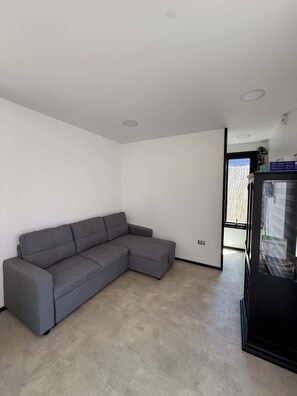 Una sala moderna con un sofá seccional gris, un mueble negro y un ventanal grande.