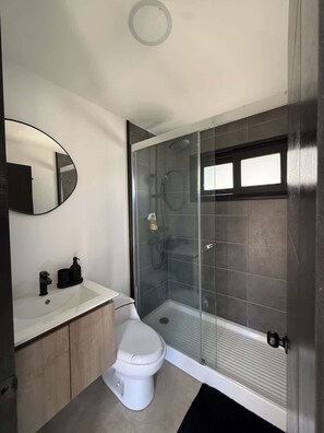 A modern bathroom with a toilet, sink, mirror, and glass-enclosed shower.
