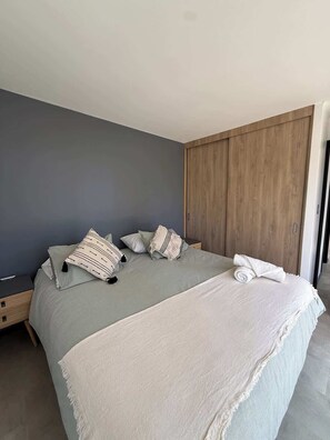 A bedroom with a bed, pillows, a blanket, a wooden wardrobe, and a nightstand.