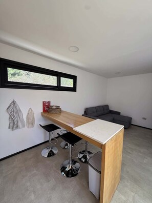 Une cuisine moderne avec un plan de travail en bois, des tabourets de bar, un canapé gris et une fenêtre donnant sur un beau paysage.