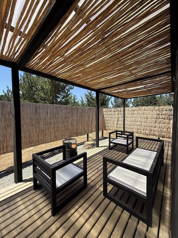 A covered outdoor patio with wooden furniture and a fire pit.
