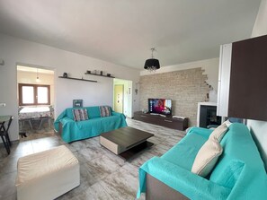 Een moderne woonkamer met een zithoek, een salontafel, een televisie en een keuken in de achtergrond.