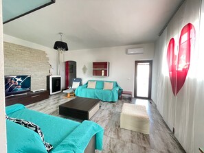 Una sala de estar con televisor, dos sofás, una mesa de centro, un mueble para televisor y una pared decorada con un corazón.