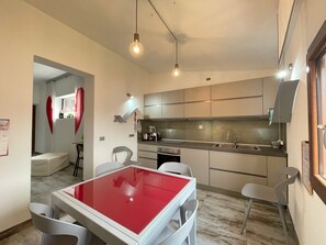 Une cuisine moderne avec un coin repas, comprenant une table avec un plateau rouge, des chaises blanches et une lampe suspendue.