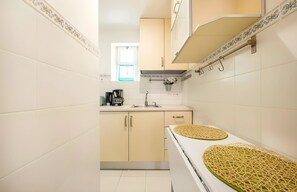 A kitchen with white tiles, a sink, cabinets, and a stove with a woven mat on it. - Historic Typical 2 By Gt House (Lisbon)