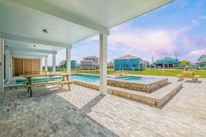 Ein überdachter Außenbereich mit Pool, Picknicktischen und Blick auf bunte Häuser.