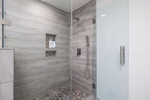 Une douche avec une porte en verre, un pommeau de douche à main et un sol carrelé.