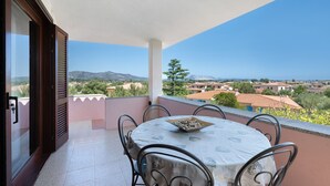 Un balcon avec une table et des chaises, donnant sur un quartier résidentiel avec des maisons et des montagnes.