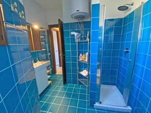 Un bagno con piastrelle blu, una doccia e un lavabo con articoli da toilette.