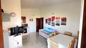 Un ambiente compatto con angolo cottura, divano, tavolo da pranzo e TV.