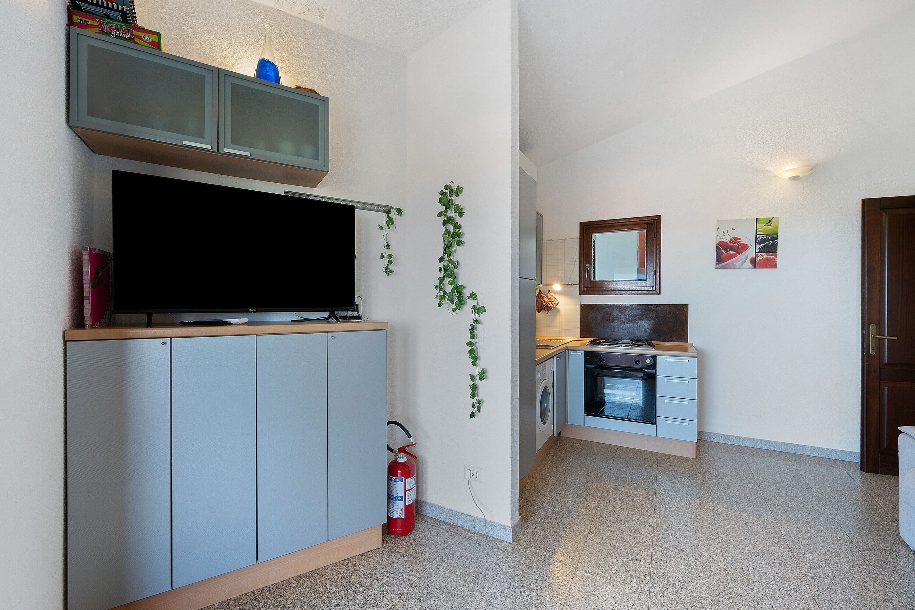 Cocina compacta con horno empotrado, lavadora y televisor sobre un mueble.