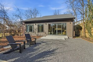 Ein modernes Haus mit Terrasse, zwei Adirondack-Stühlen und einer Schotterauffahrt.