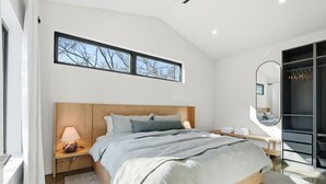 Une chambre à coucher moderne avec un lit en bois, une table de chevet, une commode, un banc, une fenêtre donnant sur un beau paysage et un dressing.