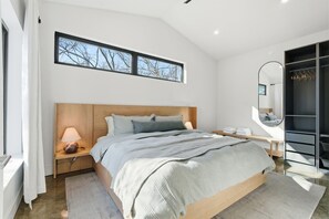 Ein modernes Schlafzimmer mit einem hölzernen Bett, einem Nachttisch, einer Sitzbank, einem Fenster mit Blick und einem begehbaren Kleiderschrank.
