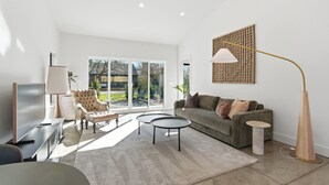 Un salon moderne avec un canapé, deux tables d’appoint, un téléviseur et une grande fenêtre.