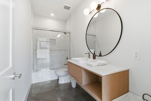 Ein modernes Badezimmer mit Duschkabine aus Glas, einer weißen Toilette, einem Waschbecken mit Spiegel und einer Holz-Kommode.