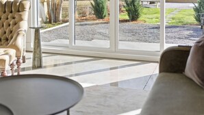 Un salon moderne avec un canapé, une table ronde et une grande porte vitrée donnant sur un espace extérieur agrémenté d’un chemin de gravier et de verdure.
