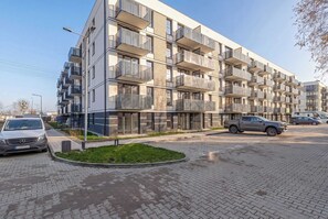 Ein mehrgeschossiges Wohngebäude mit Balkonen, einer gepflasterten Auffahrt und abgestellten Autos.