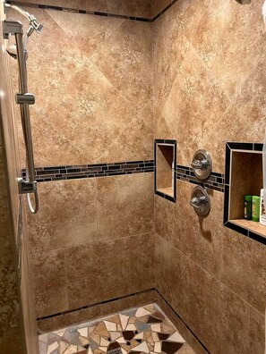 Eine Dusche mit Duschbrause, Wandarmatur und gefliestem Boden.