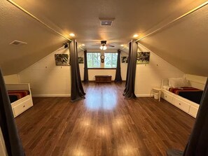 Ein Zimmer mit schrägen Wänden, Holzdielen, einem Deckenventilator, einem Fenster mit Blick und einem Bett mit Kopfteil.