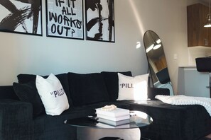 Ein modernes Wohnzimmer mit einer schwarzen Couch, einem Glastisch und einem Surfbrett, das an der Wand lehnt.