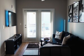 Een woonkamer met een bank, een salontafel, een televisie aan de muur en een schuifdeur naar een balkon.